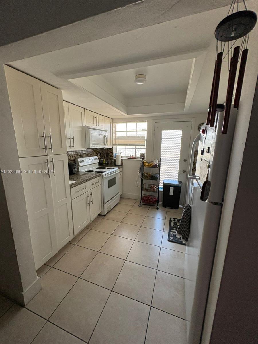 A galley kitchen features white cabinets, tile flooring, a stove, and a back door — 11840 NE 19th Dr # 14, North Miami FL 33181, NORTH MIAMI, FL