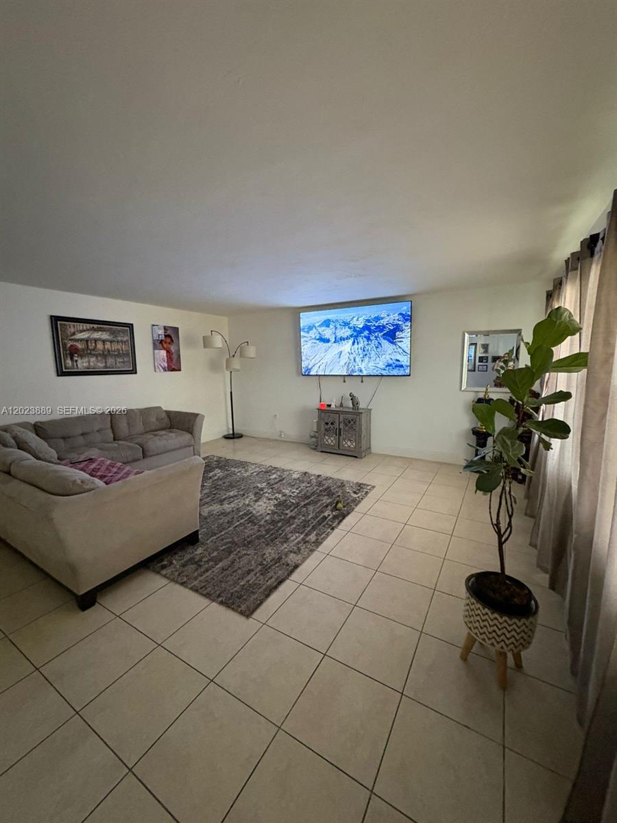 A living room features a large sectional sofa, a wall-mounted television, and tile flooring — 11840 NE 19th Dr # 14, North Miami FL 33181, NORTH MIAMI, FL