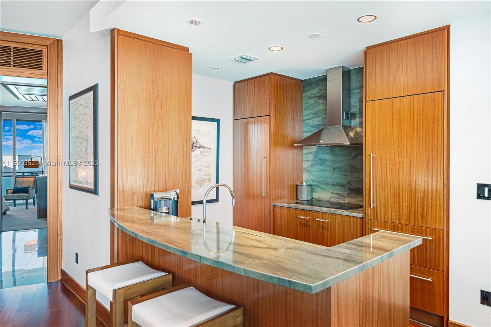 A modern kitchen features wood cabinetry, a stone countertop, and a stainless steel range hood — 10295 Collins Ave # 121716, Bal Harbour FL 33154, BAL HARBOUR, FL