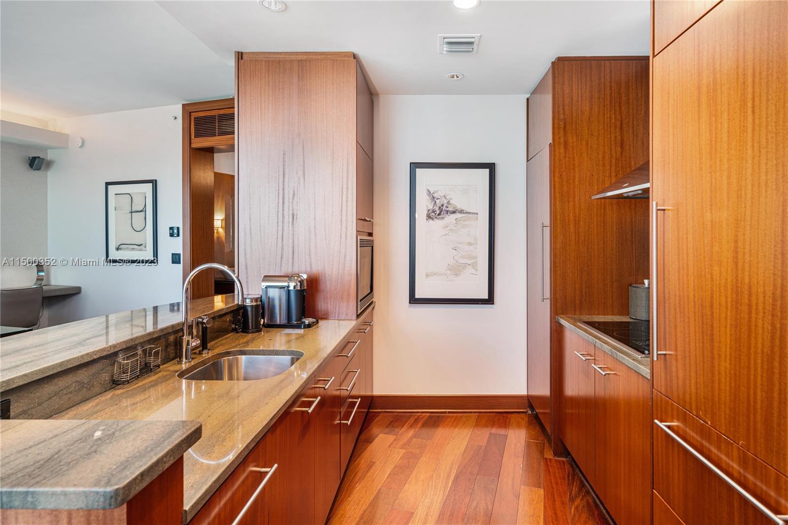A kitchen features wood cabinetry, granite countertops, stainless steel appliances, and hardwood flooring — 10295 Collins Ave # 121716, Bal Harbour FL 33154, BAL HARBOUR, FL