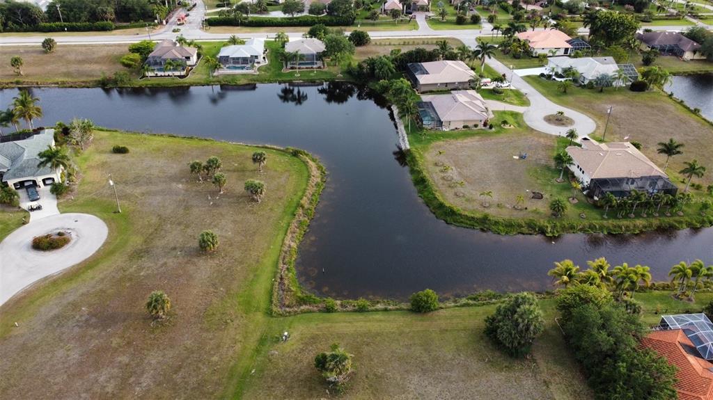 An aerial view shows a residential neighborhood with houses surrounding a central pond — 23999 CEDAR RAPIDS ROAD, PUNTA GORDA, FL
