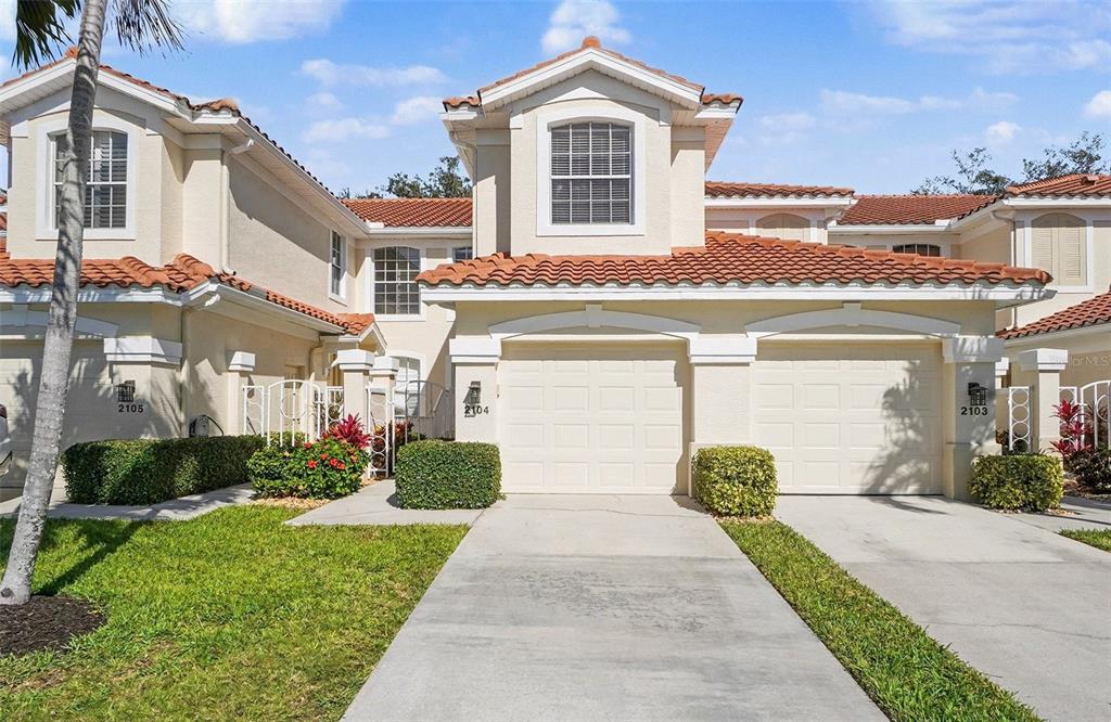 A two-story townhouse exterior with a beige stucco facade, tile roof, and two garage doors — 11270 JACANA COURT UNIT 2104, FORT MYERS, FL