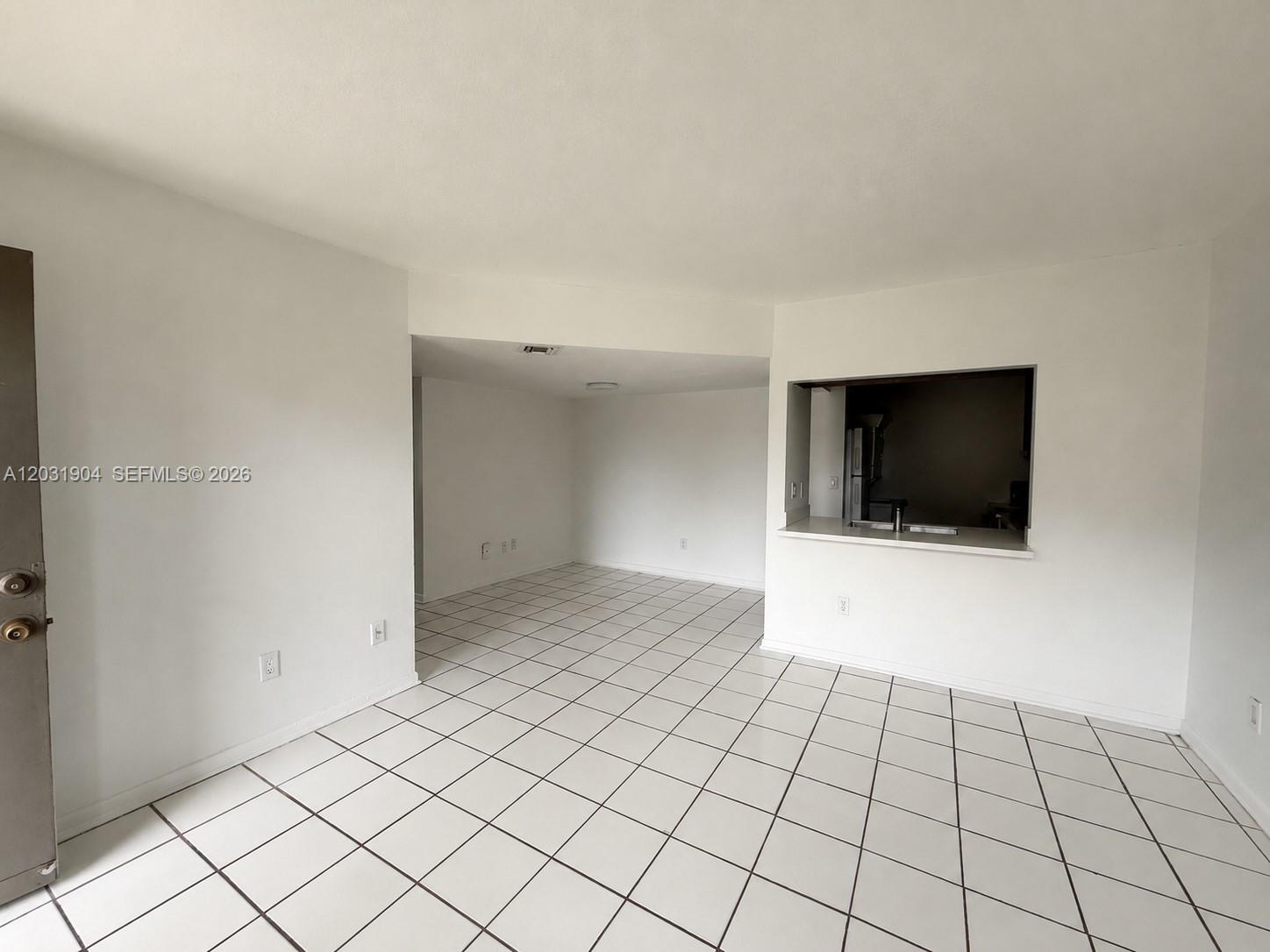 An empty room with white walls, white tiled floors, and a kitchen pass-through window — 15316 SW 72nd St # 14, Miami FL 33193, MIAMI, FL