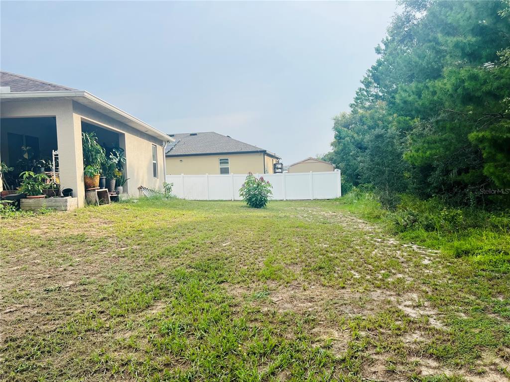 A view of a grassy backyard with a covered patio and a white vinyl fence — 231 ELM COURT, KISSIMMEE, FL