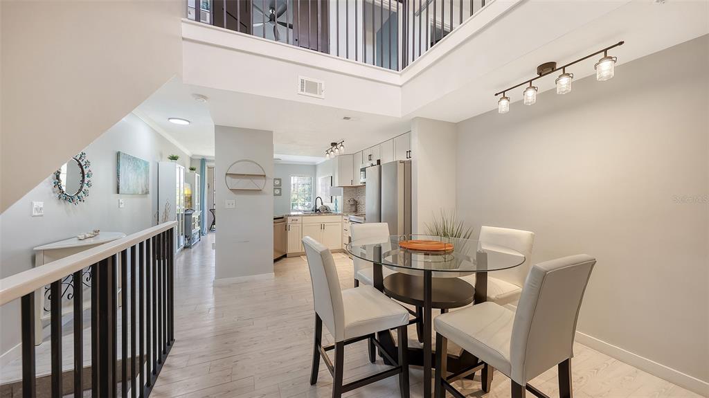 A dining area with a glass table and white chairs sits beneath a modern light fixture — 5655 BENTGRASS DRIVE UNIT 9-116, SARASOTA, FL