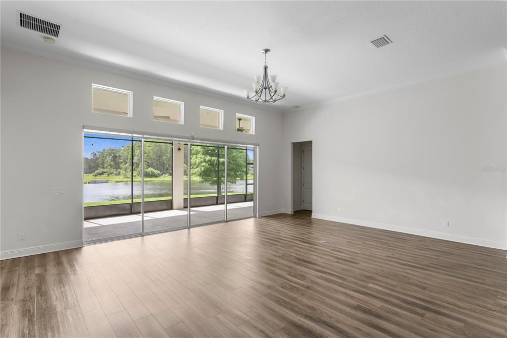 A spacious living room features wood-look flooring, a chandelier, and sliding glass doors overlooking water — 2160 SECRET COVE, ODESSA, FL