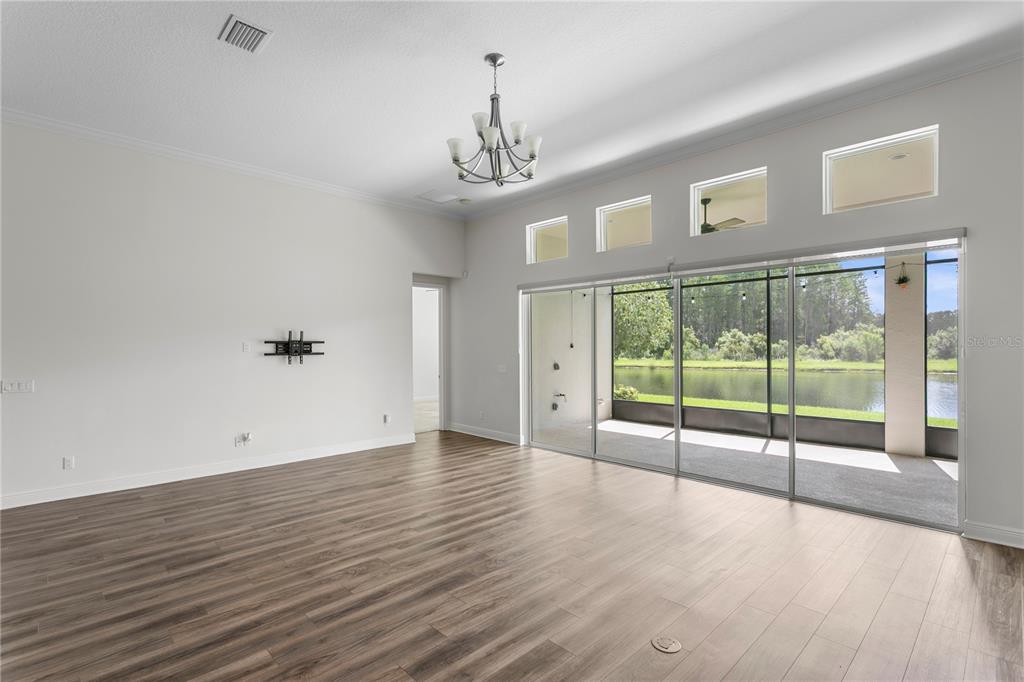 A spacious living room features wood-look flooring, a chandelier, and sliding glass doors overlooking a lake — 2160 SECRET COVE, ODESSA, FL