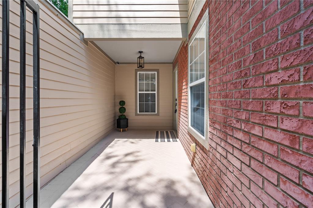 A covered entryway features a brick wall, beige siding, a window, and a potted topiary — 1215 NW 55TH STREET NW UNIT 7, GAINESVILLE, FL