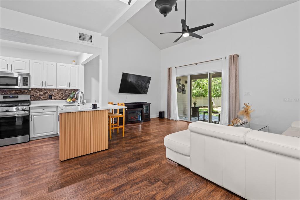 An open-concept living room and kitchen feature white cabinets, wood flooring, and vaulted ceilings — 1215 NW 55TH STREET NW UNIT 7, GAINESVILLE, FL