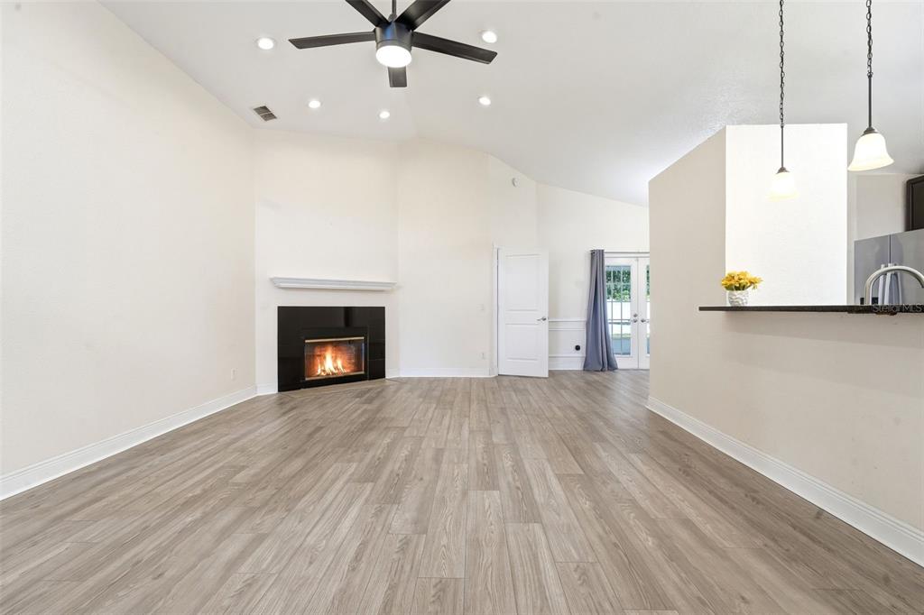 A living room features light wood-look flooring, a corner fireplace, and a ceiling fan — 1238 COURTLAND BOULEVARD, DELTONA, FL