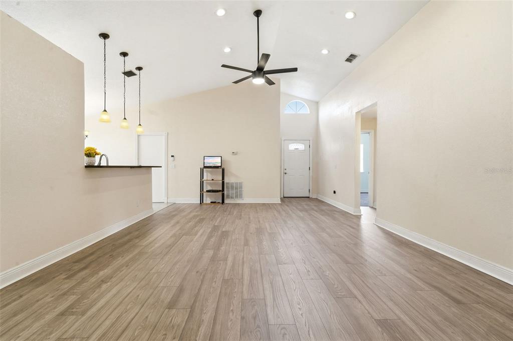 A spacious living room features light wood-look flooring, a vaulted ceiling, and a ceiling fan — 1238 COURTLAND BOULEVARD, DELTONA, FL