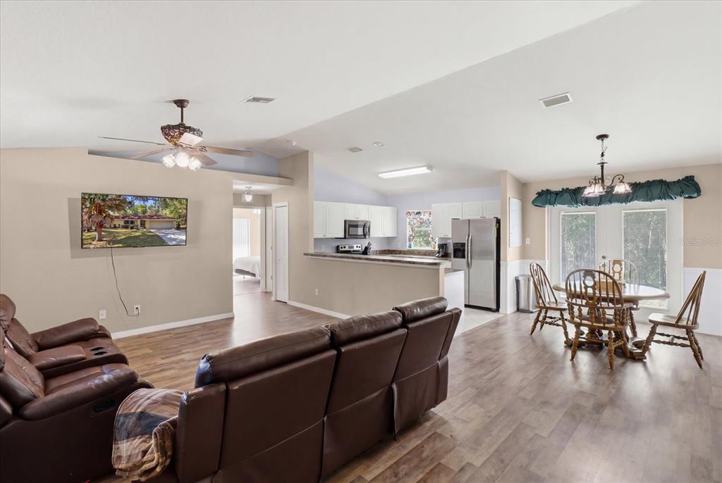 An open-concept living room and kitchen feature wood-look flooring, brown leather furniture, and dining area — 3220 E ROGERS STREET, INVERNESS, FL