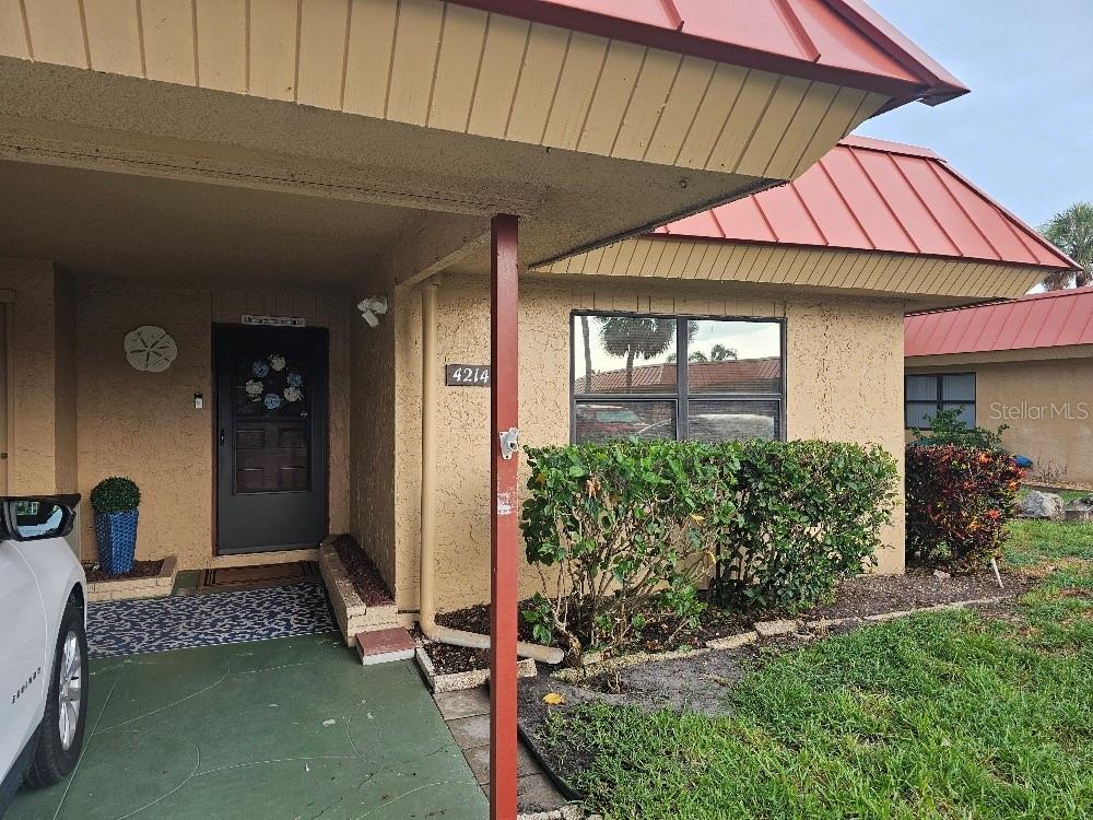 A tan stucco house exterior features a red metal roof and a covered front entryway — 4214 EL DORADO COVE UNIT V-10, BRADENTON, FL
