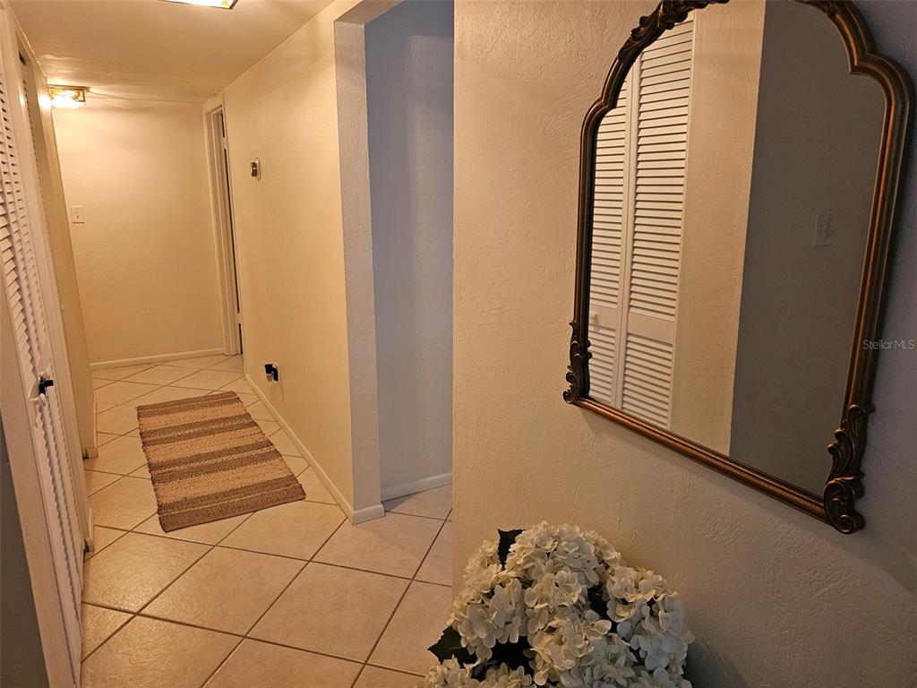 A hallway with tiled floors, a decorative mirror, and a small floral arrangement — 4214 EL DORADO COVE UNIT V-10, BRADENTON, FL