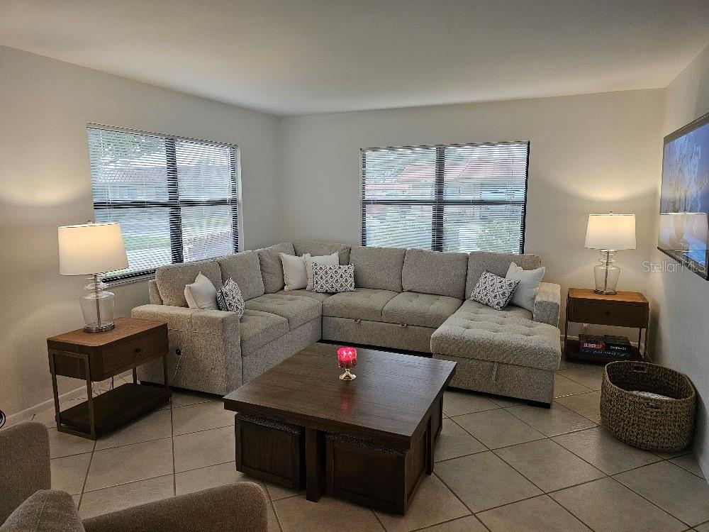 A living room features a large gray sectional sofa, a wooden coffee table, and windows — 4214 EL DORADO COVE UNIT V-10, BRADENTON, FL