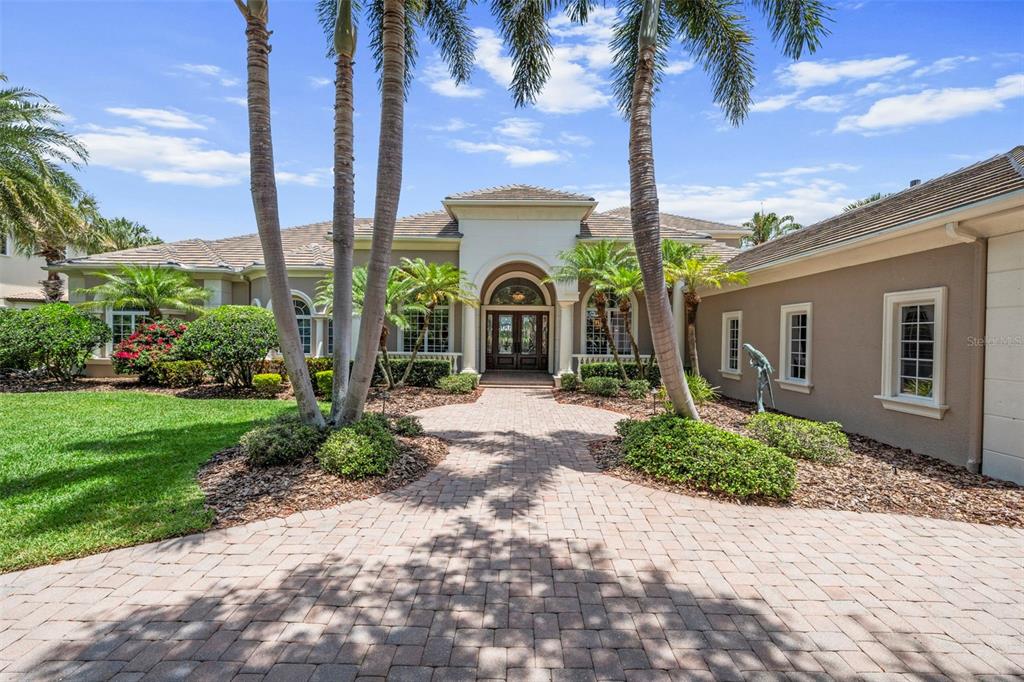 A paved walkway leads to the arched entryway of a tan house with palm trees — 4085 FOUNDERS CLUB DRIVE, SARASOTA, FL