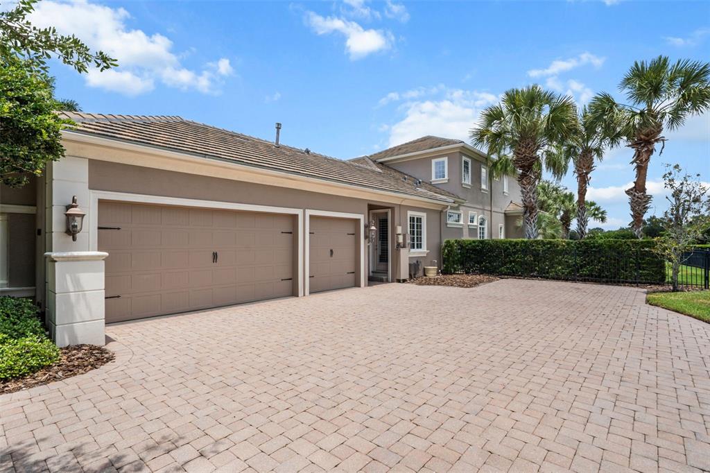 A tan house with a three-car garage and a paved driveway under a blue sky — 4085 FOUNDERS CLUB DRIVE, SARASOTA, FL