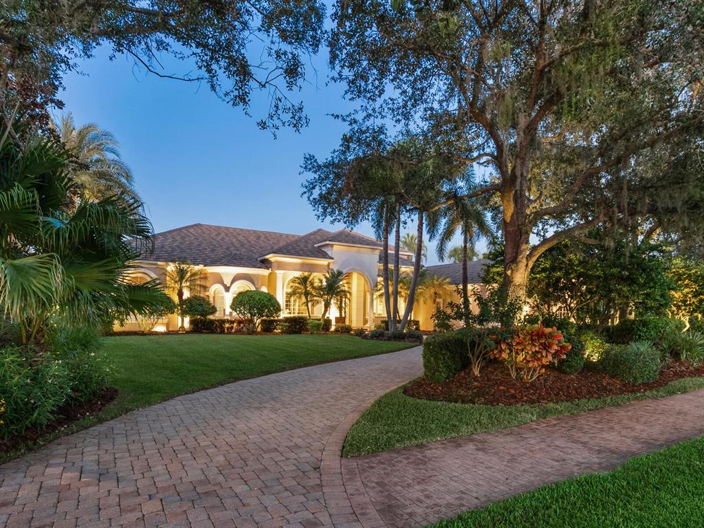 A single-story house with a paved driveway and lush landscaping at twilight — 4085 FOUNDERS CLUB DRIVE, SARASOTA, FL