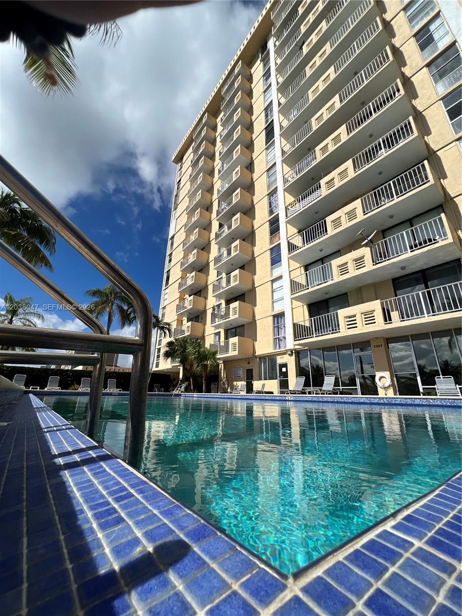 A swimming pool sits in front of a tall, multi-story residential building with balconies — 2350 NE 135th St # 704, North Miami FL 33181, NORTH MIAMI, FL