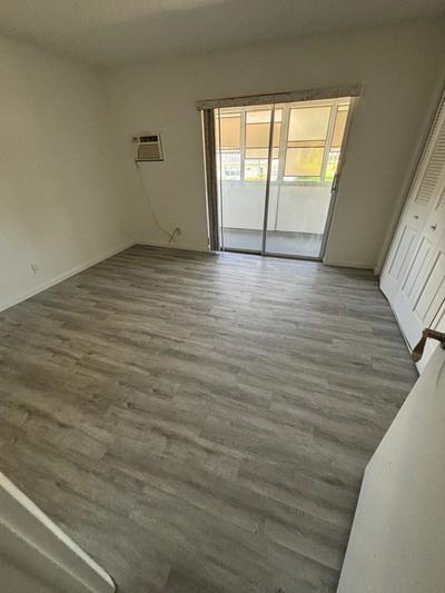 A bedroom with light gray wood-look flooring, a sliding glass door, and a wall-mounted air conditioner — 244 Windsor K, West Palm Beach FL 33417, WEST PALM BEACH, FL