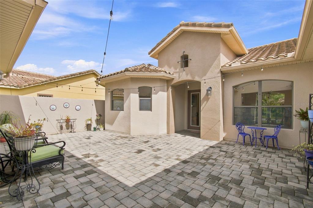 A paved patio area sits outside a tan stucco house with a tiled roof — 970 SAN RAPHAEL STREET, POINCIANA, FL