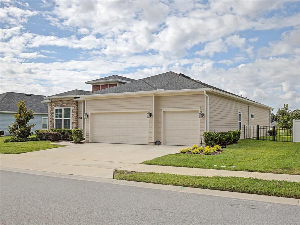 A tan-sided house with a three-car garage and a stone facade sits on a corner lot — 7672 SW 74TH LOOP, OCALA, FL