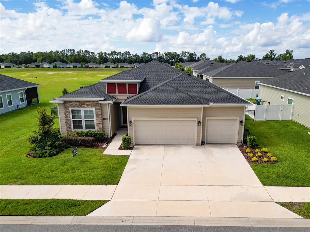 An aerial view of a single-story suburban house with a tan exterior and three-car garage — 7672 SW 74TH LOOP, OCALA, FL