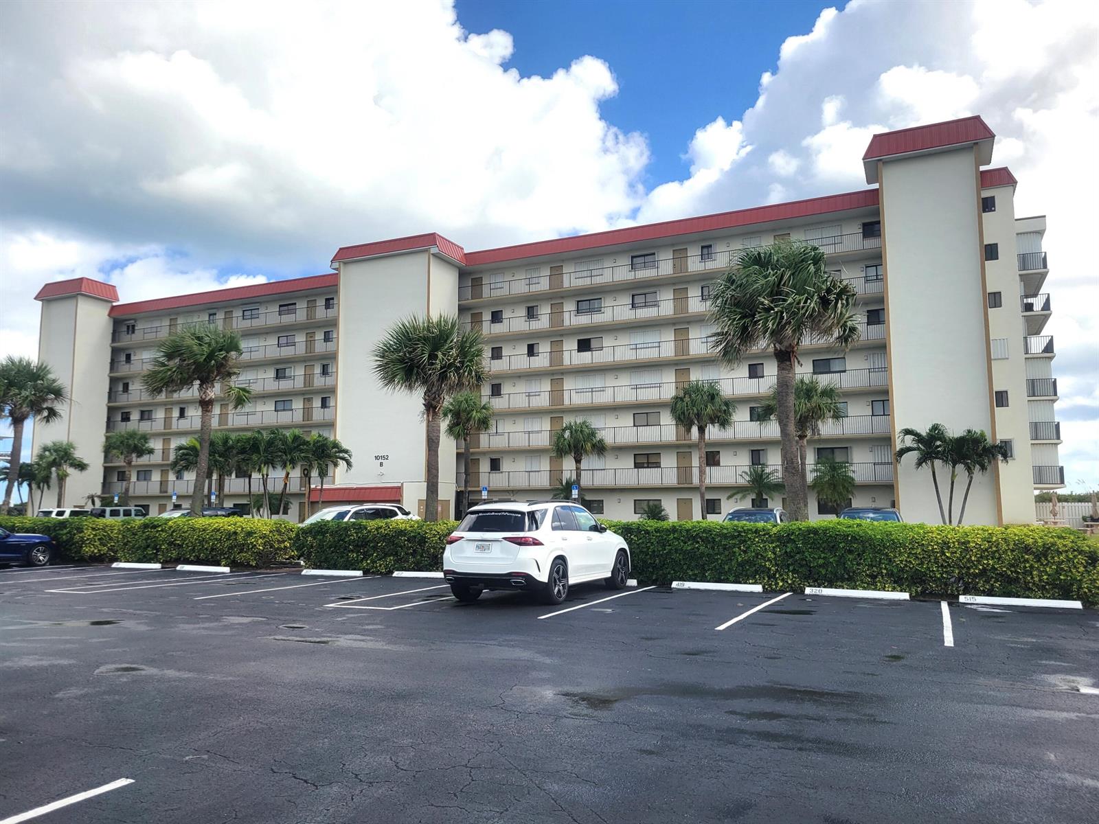 A multi-story apartment building with a red roof stands behind a parking lot — 10152 S Ocean Drive # 418b, Jensen Beach FL 34957, JENSEN BEACH, FL