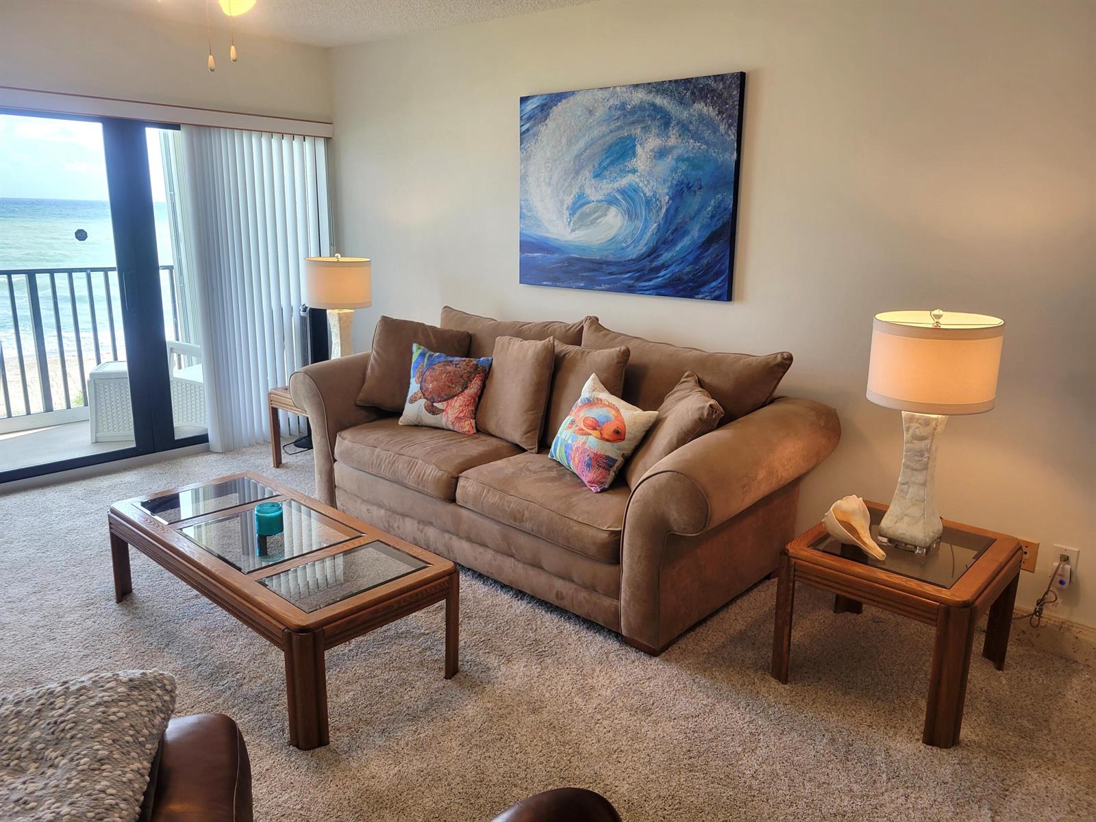 A living room features a brown sofa, glass-top wooden tables, and a large ocean painting — 10152 S Ocean Drive # 418b, Jensen Beach FL 34957, JENSEN BEACH, FL