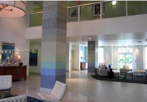 A bright, modern lobby features tiled columns, white furniture, and a second-floor mezzanine balcony — 2000 N Bayshore Dr # 122, Miami FL 33137, MIAMI, FL