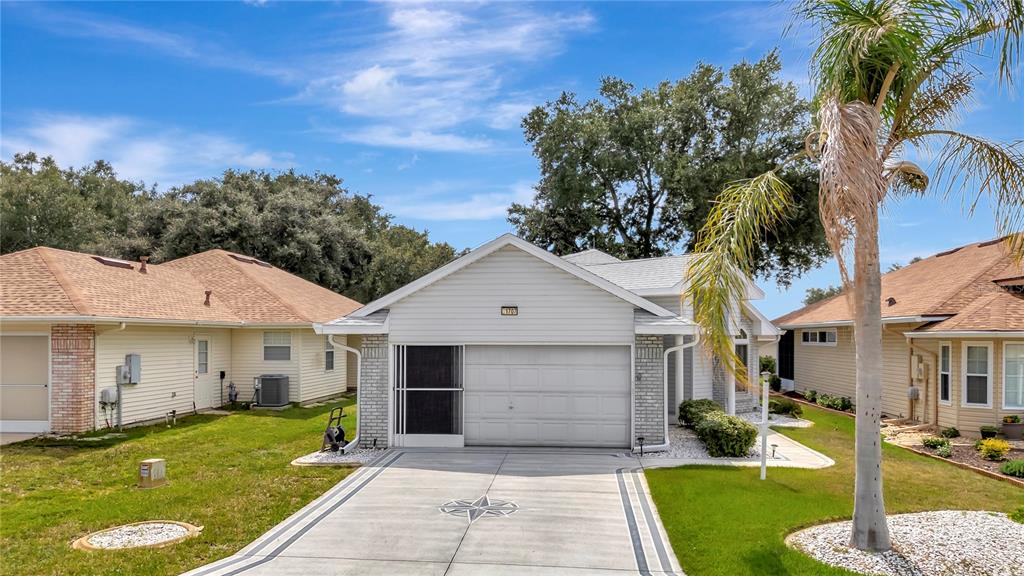 A single-story house with a white garage, light siding, and a concrete driveway with accents — 21707 QUEEN MARY COURT, LEESBURG, FL