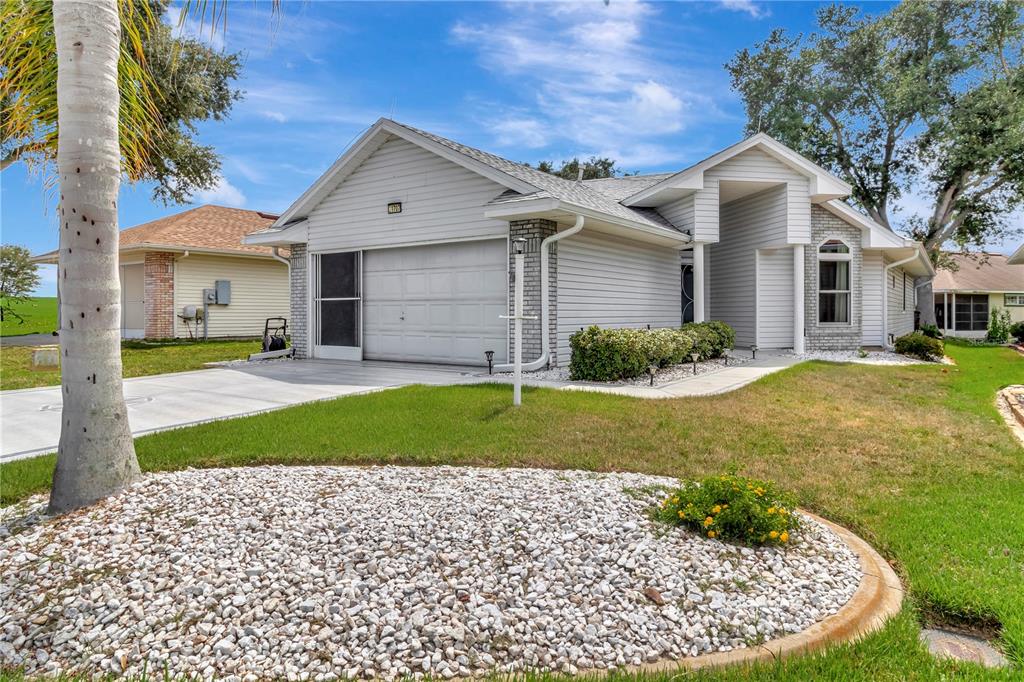 A single-story house with light gray siding, a two-car garage, and a white rock garden — 21707 QUEEN MARY COURT, LEESBURG, FL