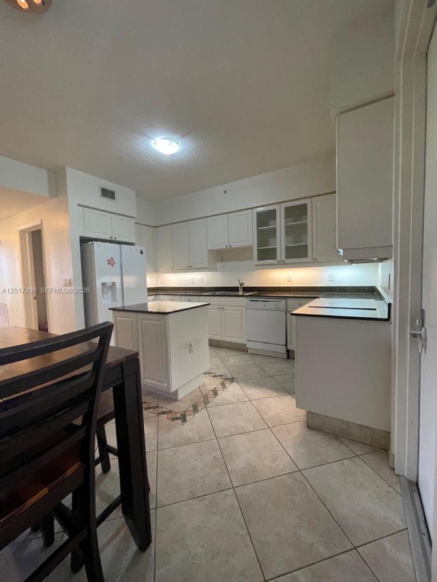 A kitchen features white cabinets, a small island, tile flooring, and white appliances — 717 Crandon Blvd # 408, Key Biscayne FL 33149, KEY BISCAYNE, FL