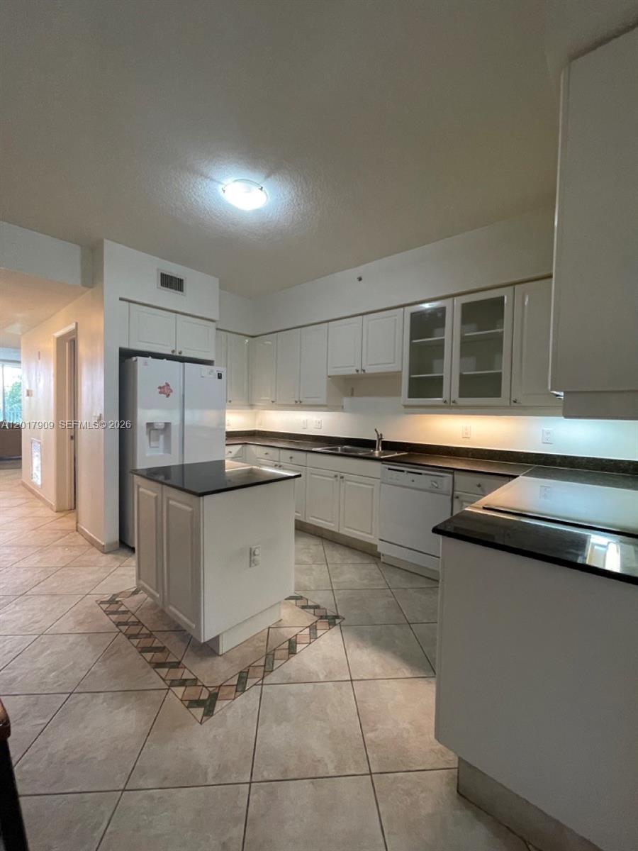 A kitchen features white cabinets, black countertops, a central island, and tiled flooring — 717 Crandon Blvd # 408, Key Biscayne FL 33149, KEY BISCAYNE, FL