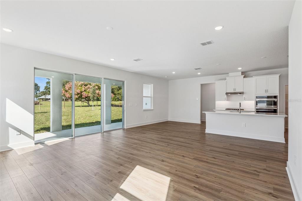 An open-concept living area with wood-look flooring, a white kitchen, and large sliding glass doors — 574 EMERALD GROVE DRIVE, APOPKA, FL