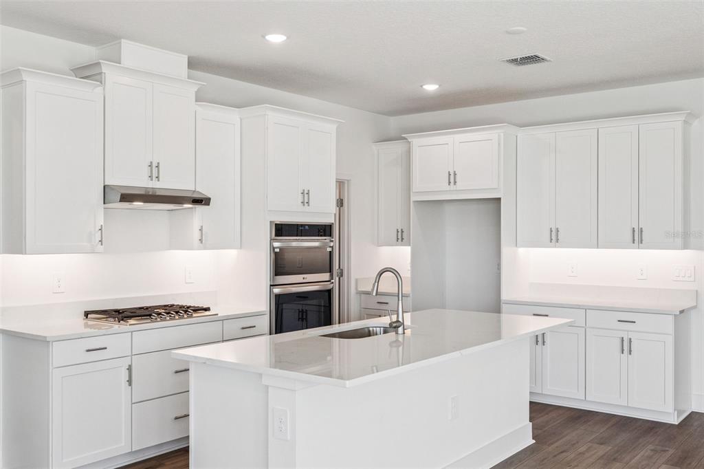 A modern kitchen features white cabinetry, quartz countertops, a center island, and stainless steel appliances — 574 EMERALD GROVE DRIVE, APOPKA, FL