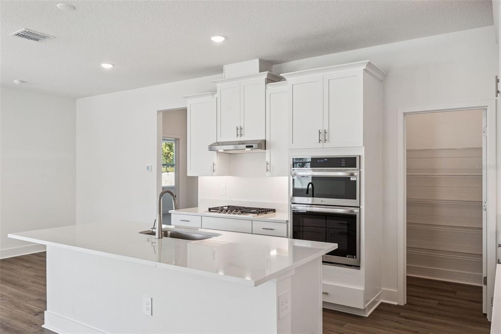 A modern kitchen features white cabinets, a quartz island with a sink, and stainless steel appliances — 574 EMERALD GROVE DRIVE, APOPKA, FL