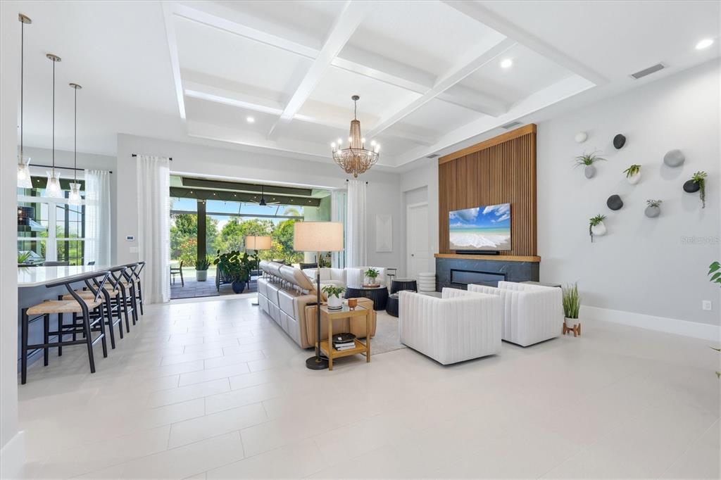 A bright open-concept living room features a coffered ceiling, fireplace, and sliding glass patio doors — 8254 PAVIA WAY, LAKEWOOD RANCH, FL