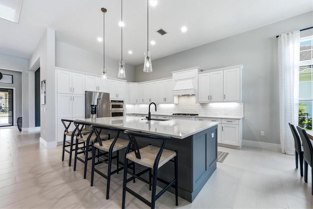 A modern kitchen features white cabinetry, a dark gray island with bar stools, and pendant lighting — 8254 PAVIA WAY, LAKEWOOD RANCH, FL