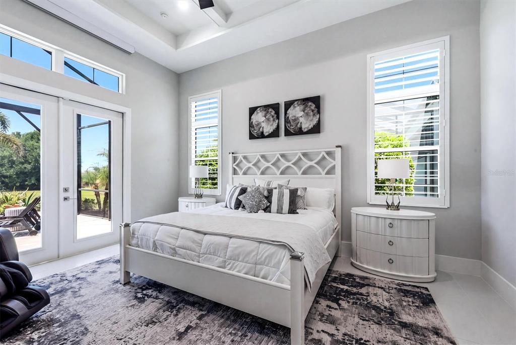 A bright bedroom features a white bed, two nightstands, and glass doors leading to a patio — 8254 PAVIA WAY, LAKEWOOD RANCH, FL