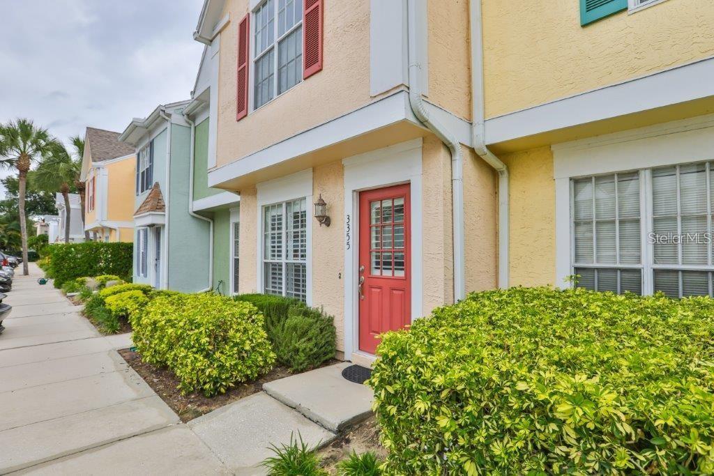 A yellow townhouse exterior features a red front door, white trim, and a landscaped walkway — 3355 W WYOMING CIRCLE, TAMPA, FL