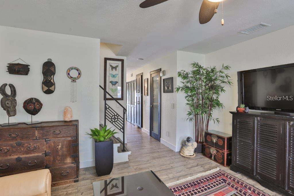 A living room features wood-look flooring, a wooden dresser, a television, and a hallway staircase — 3355 W WYOMING CIRCLE, TAMPA, FL