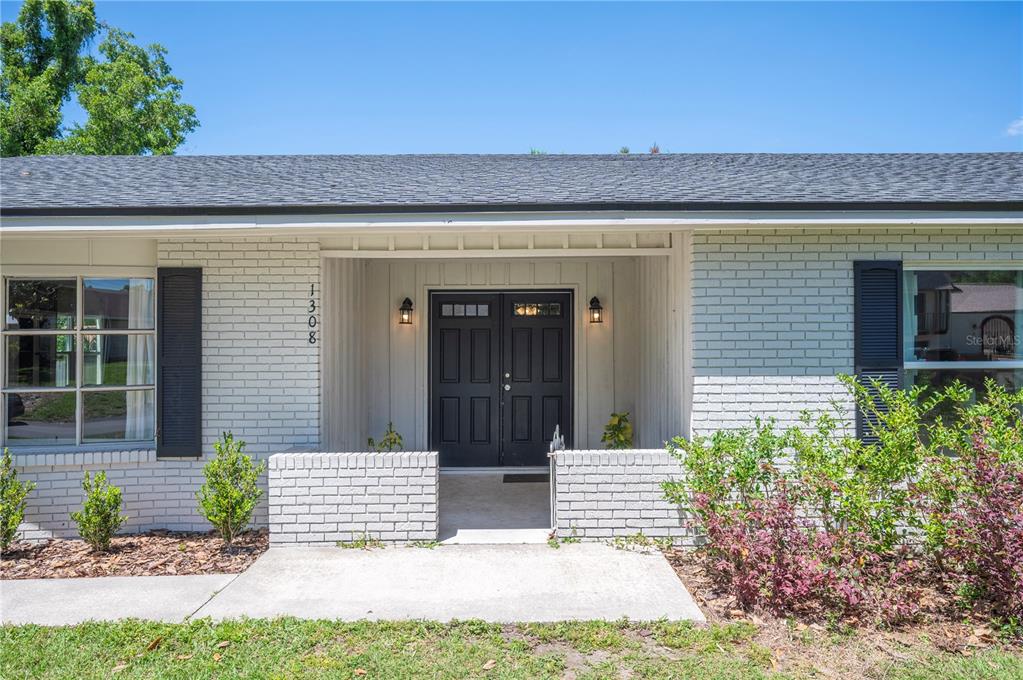 A white brick house exterior features a recessed entryway with double black doors — 1308 GLENFORD LANE, LAKELAND, FL