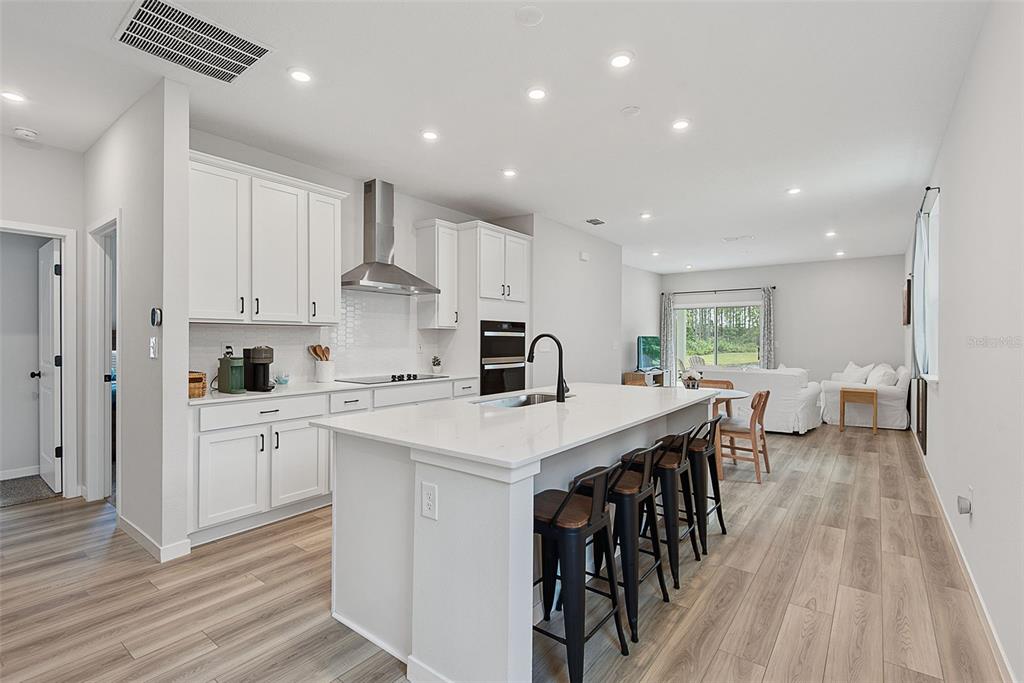 A modern kitchen features white cabinetry, a large island with bar stools, and light flooring — 1303 RIBBON PLACE, PALM COAST, FL