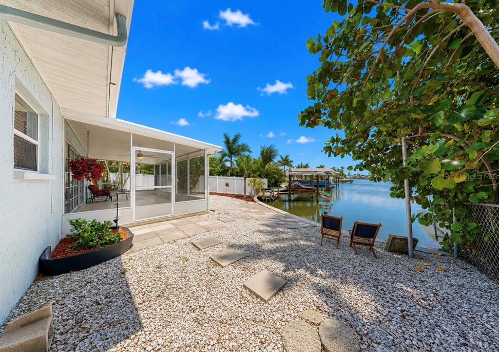 A gravel backyard with a screened-in patio overlooks a canal with a private boat dock — 6513 ABACO DRIVE, APOLLO BEACH, FL