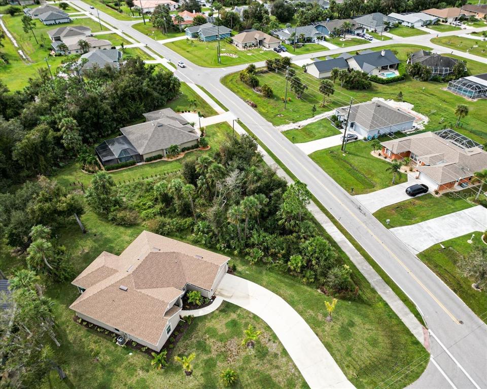 An aerial view shows a suburban neighborhood with single-family homes, paved streets, and wooded areas — 25655 DEEP CREEK BOULEVARD, PUNTA GORDA, FL