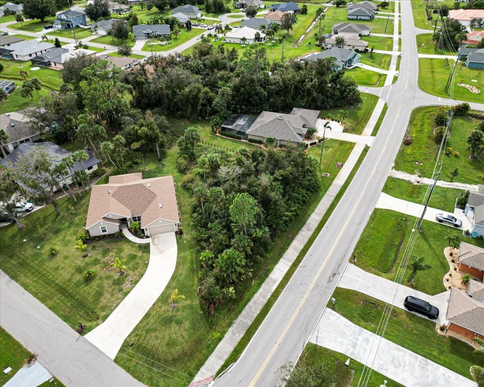 An aerial view shows a suburban neighborhood with houses, driveways, and a wooded lot — 25655 DEEP CREEK BOULEVARD, PUNTA GORDA, FL