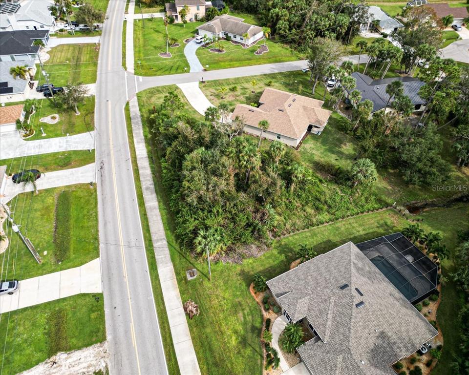 An aerial view shows a residential street with several houses and a wooded vacant lot — 25655 DEEP CREEK BOULEVARD, PUNTA GORDA, FL