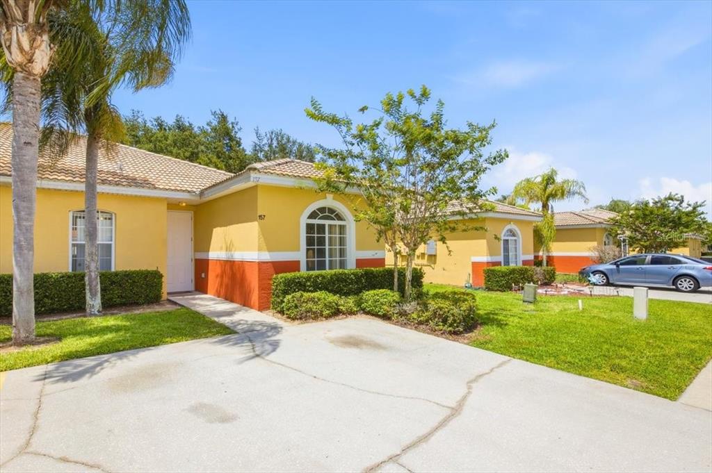 A yellow single-story house with a concrete driveway, green lawn, and palm trees — 157 OCEAN BLUFF DRIVE, POINCIANA, FL