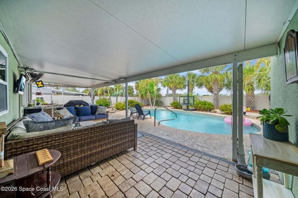 A covered patio features wicker furniture and overlooks a backyard swimming pool with palm trees — 121 Algonquin Terrace, Indian Harbour Beach FL 32937, INDIAN HARBOUR BEACH, FL